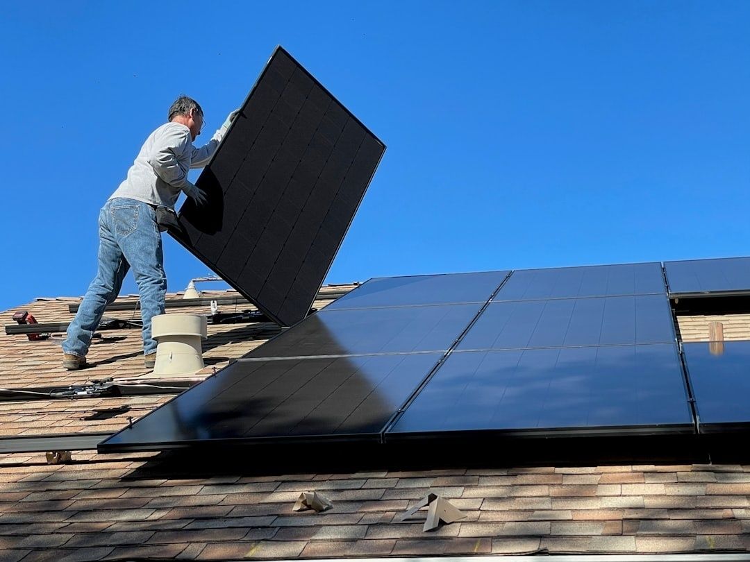 Mann montiert ein Solarmodul auf einem Hausdach mit weiteren Photovoltaikmodulen