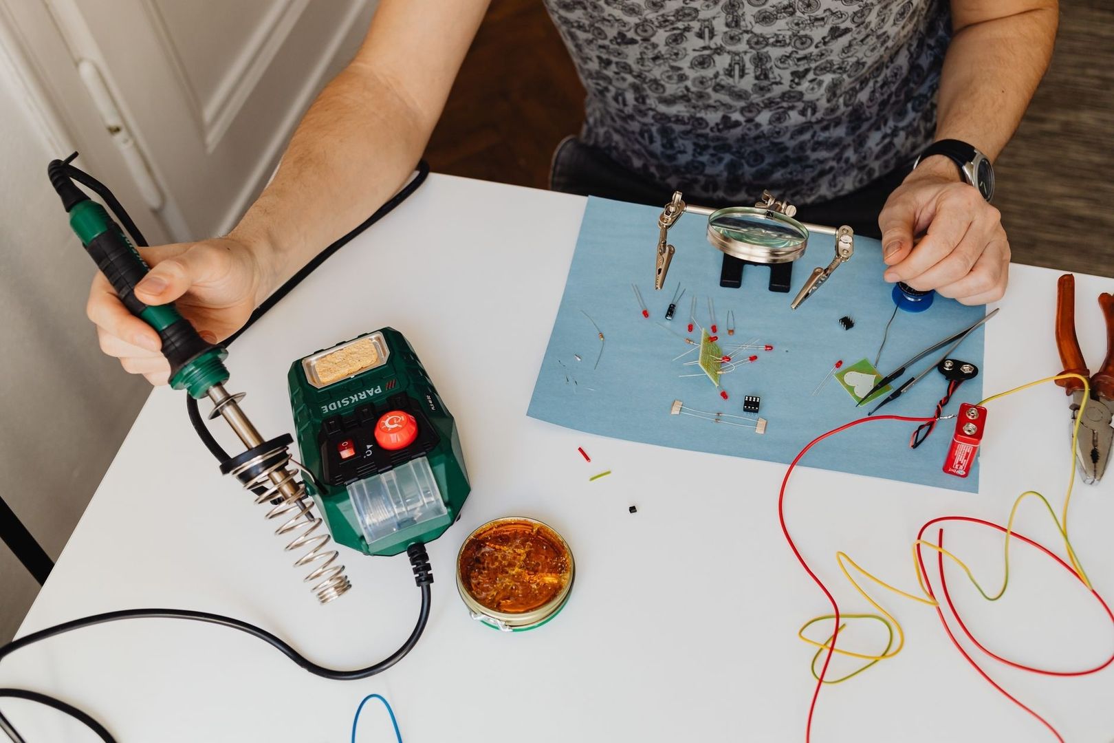 Person lötet elektronische Bauteile an einem Tisch mit Reparaturwerkzeug