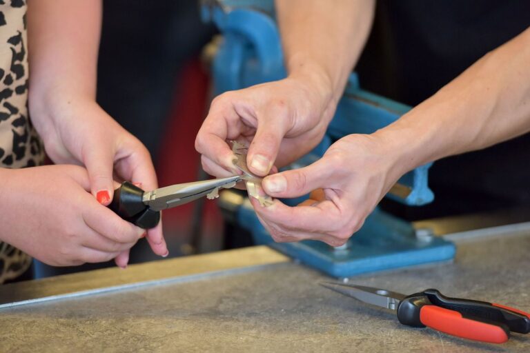 Zwei Personen reparieren gemeinsam mit Werkzeug eine kleine Metallfigur